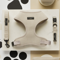 A stylish dog harness set displayed on a white background with geometric patterns. The Brown Tweed Adjustable Neck Harness, Lead & Collar Bundle by Cocopup London includes a beige herringbone fabric harness, leash, and collar, all featuring black clasps and "Cocopup London" branding labels. Perfect for chic dog walks.