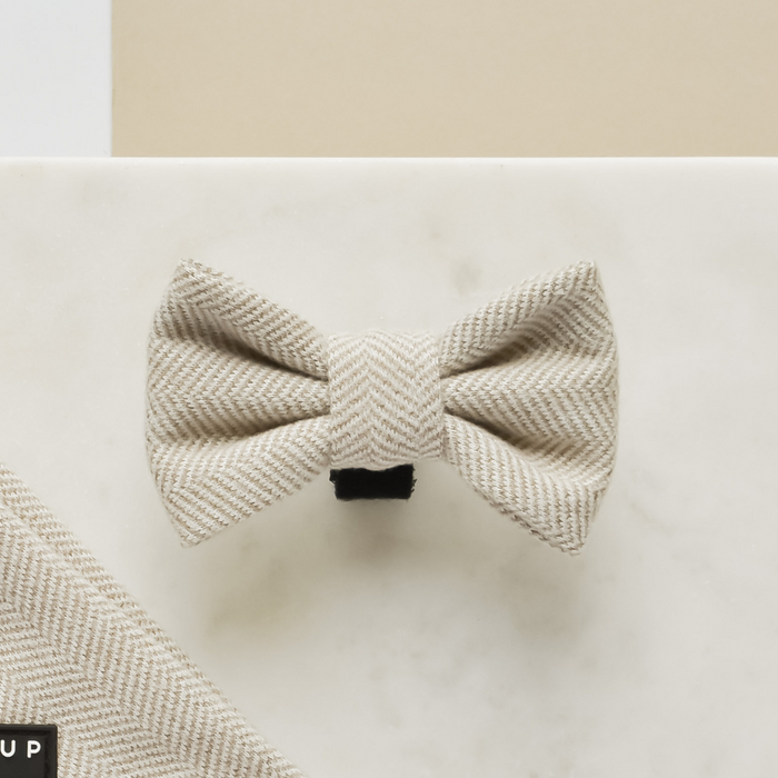 Brown tweed bow tie on light marble surface with a matching fabric swatch in the corner.