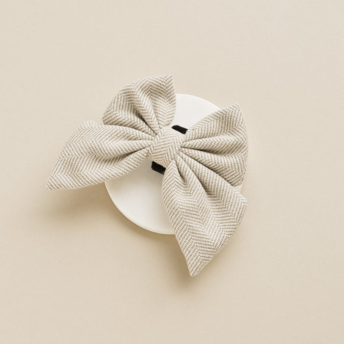 Brown tweed sailor bow tie on a round white dish, set against a light beige background.