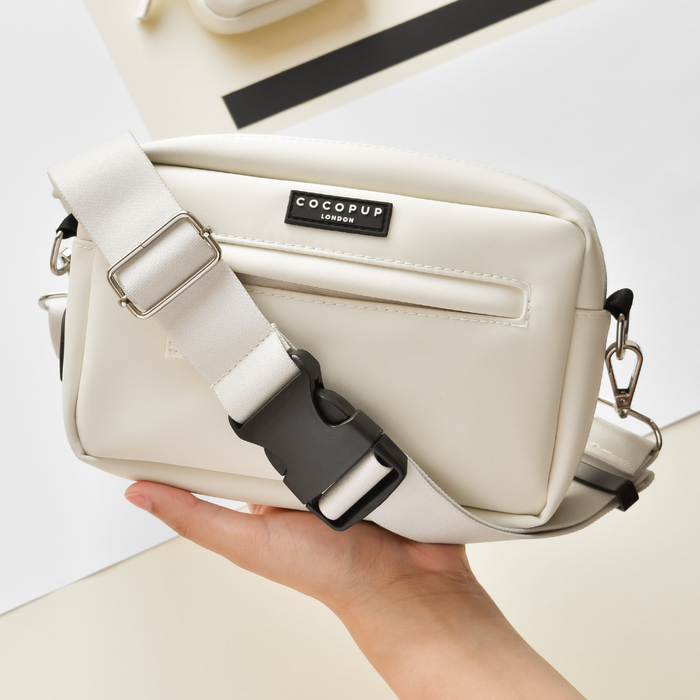 Hand holding an Oyster White Cocopup London bum bag with a white strap and black buckle.