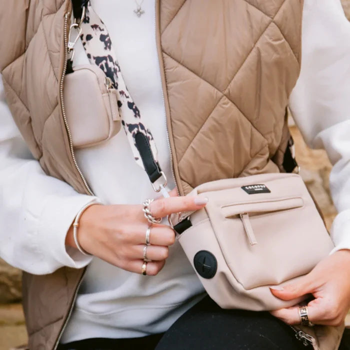 Caramel brown Cocopup London dog walking bag with treat pouch and patterned strap, held by person in a quilted vest.