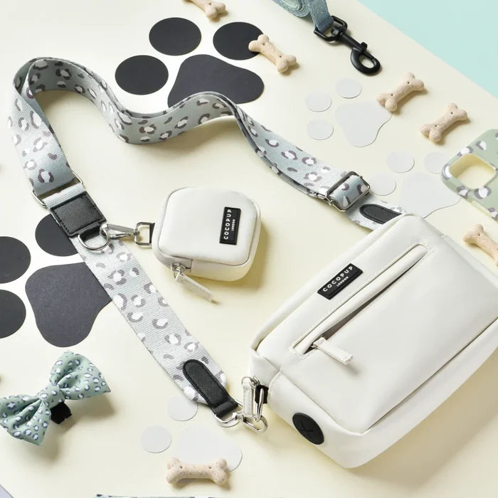 Oyster white Cocopup London dog walking bag with patterned straps, displayed alongside treats and bow ties.