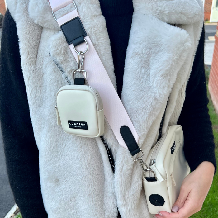 Person in grey faux fur vest with two cream Cocopup London dog walking bags, one crossbody and one clipped on.