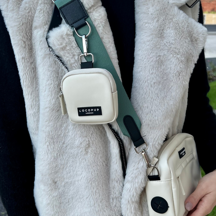 Person in a gray fluffy vest carries two white Cocopup London dog walking bags and a treat pouch on a strap.
