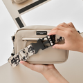 Hands fastening an ivory tortoiseshell bum bag bundle to a beige dog walking bag on a light background.