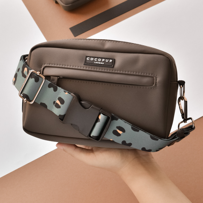 Hand holding a khaki leopard print Cocopup London bum bag against a plain background.