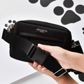 Hands holding a plain black Cocopup London bum bag with a wide strap, background features black paw prints.