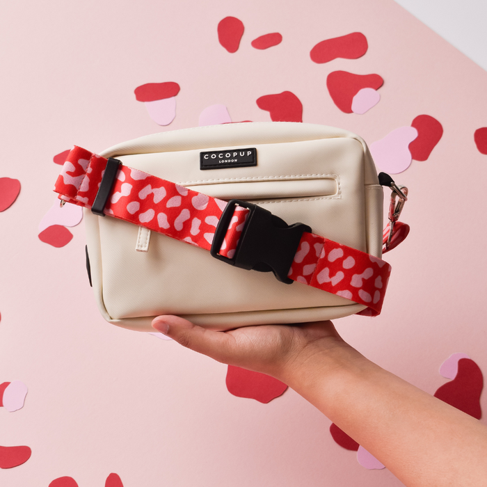 Red and pink leopard print Cocopup London bum bag with matching strap, held in a persons hand.
