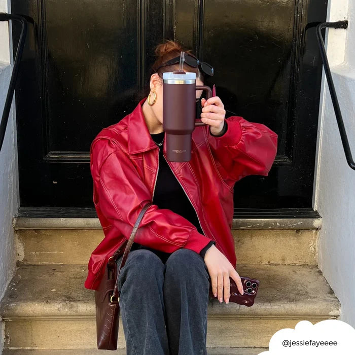 Person in a red jacket on steps holds a burgundy stainless steel tumbler.