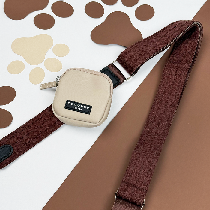 Beige Cocopup London dog walking bag with cable knit strap, Hot Coco color, on a paw print background.