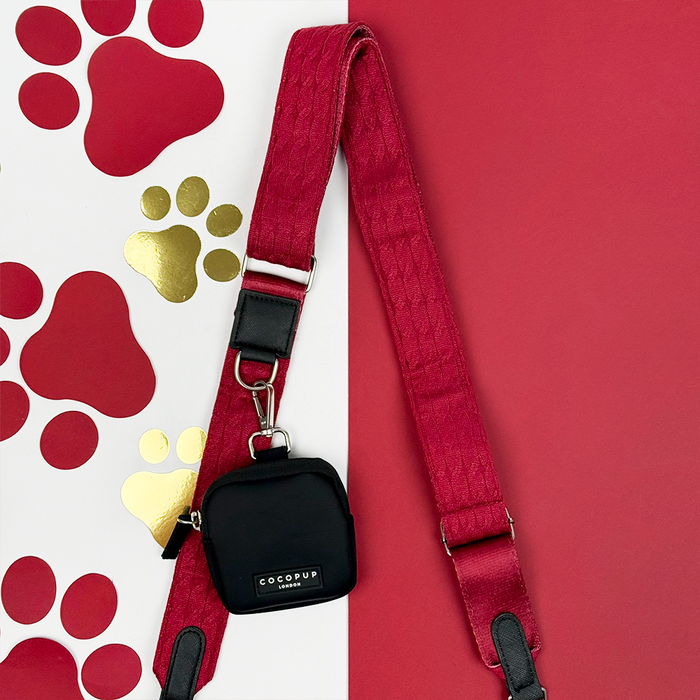 Mulled wine cable knit bag strap with black pouch, set on a red and white background with gold and red paw prints.
