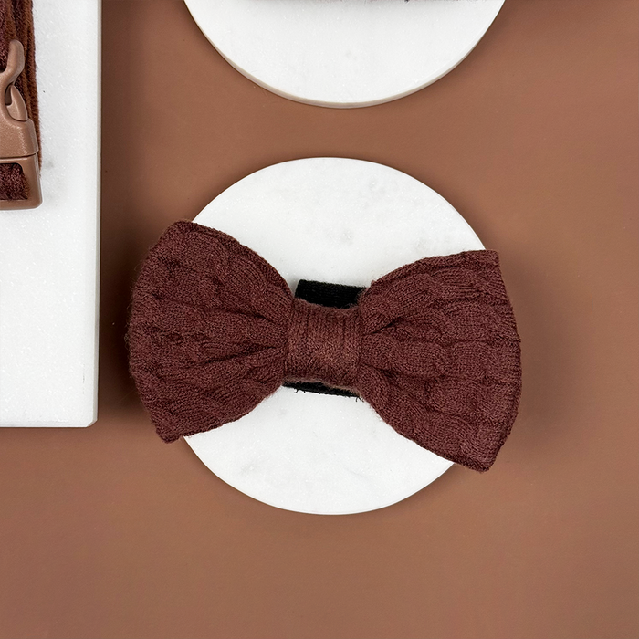 Brown cable knit bow tie for dogs displayed on a white round surface with a brown background.