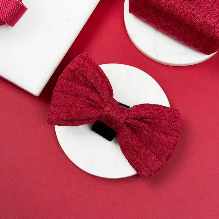 Red cable knit dog bow tie displayed on a white circle background with a red surface.
