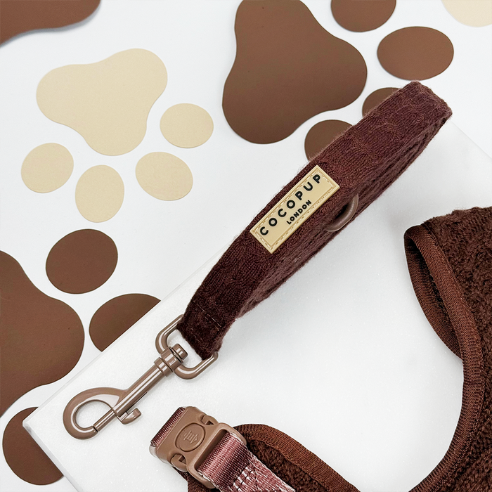 Brown cable knit dog lead for small breeds on a white surface with a brown and beige paw print background.