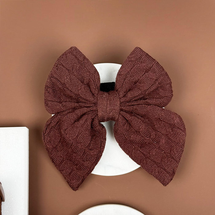 Brown cable knit sailor bow tie on a round white card, set against a brown backdrop.