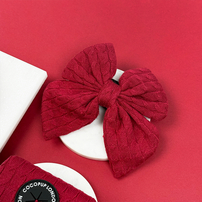 Cable knit sailor bow tie in deep red mulled wine color on a white surface with a red background.