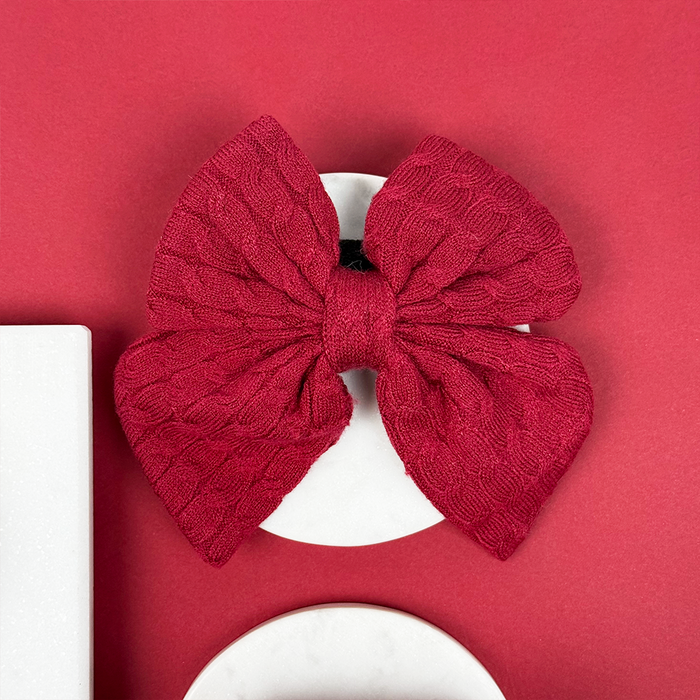 Mulled wine cable knit sailor bow tie by Cocopup London on a white round surface with a red background.
