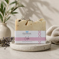Bar of soap with 'OldSoul Soap Company' packaging on a stone surface with lavender and a plant in the background.