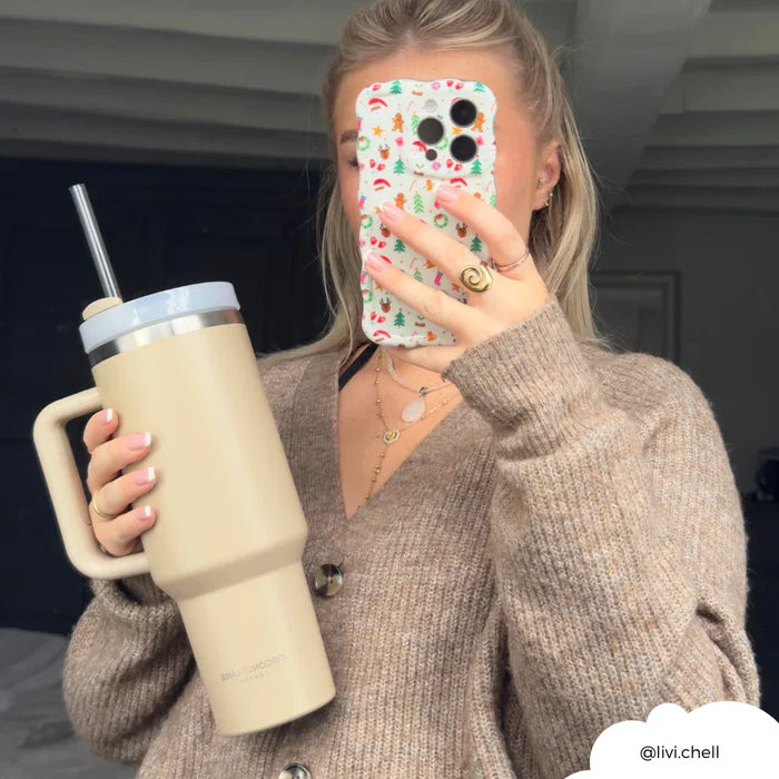 Woman in a brown sweater holds a tan Cocopup London tumbler and a floral phone case, posing for a mirror selfie.
