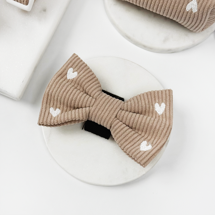 Tan ribbed bow tie with small white hearts, shown on a round white holder.