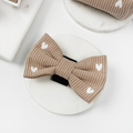 Tan ribbed bow tie with small white hearts, shown on a round white holder.