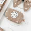Beige Cocopup London poop bag holder with white heart pattern, branded logo, and clasp on a marble background.
