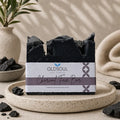 Charcoal face bar soap with packaging on a stone surface, surrounded by natural elements.