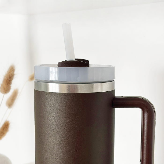 Chocolate brown stainless steel tumbler with handle and straw lid on a light surface.
