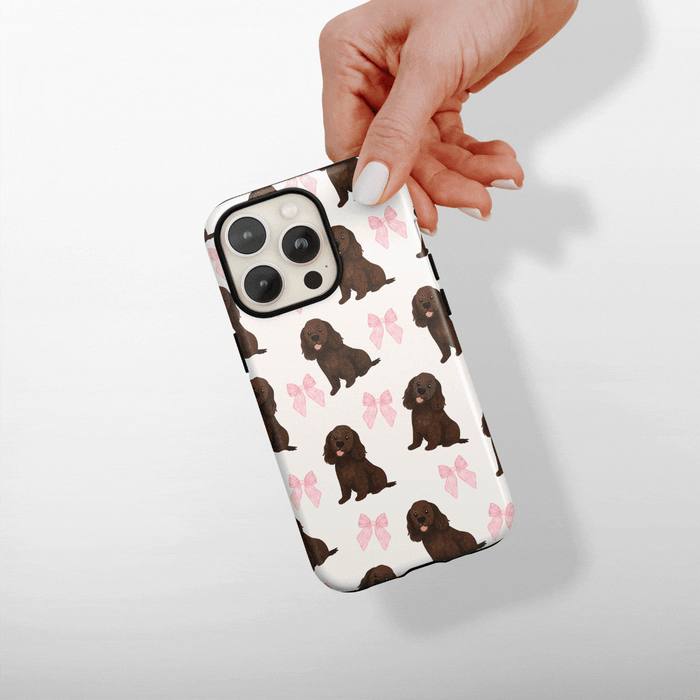 Hand holding a white phone case with brown puppy and pink bow pattern from Cocopup London.