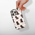 Hand holding a white phone case with brown puppy and pink bow pattern from Cocopup London.