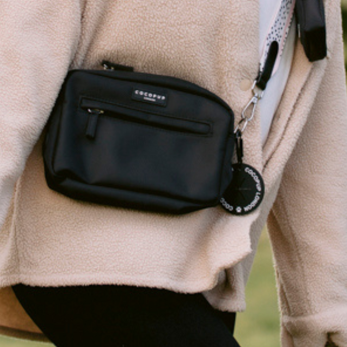 Person in a tan fleece jacket with a black Cocopup London CocoPOOP Pocket dog walking bag and built-in poop bag holder.