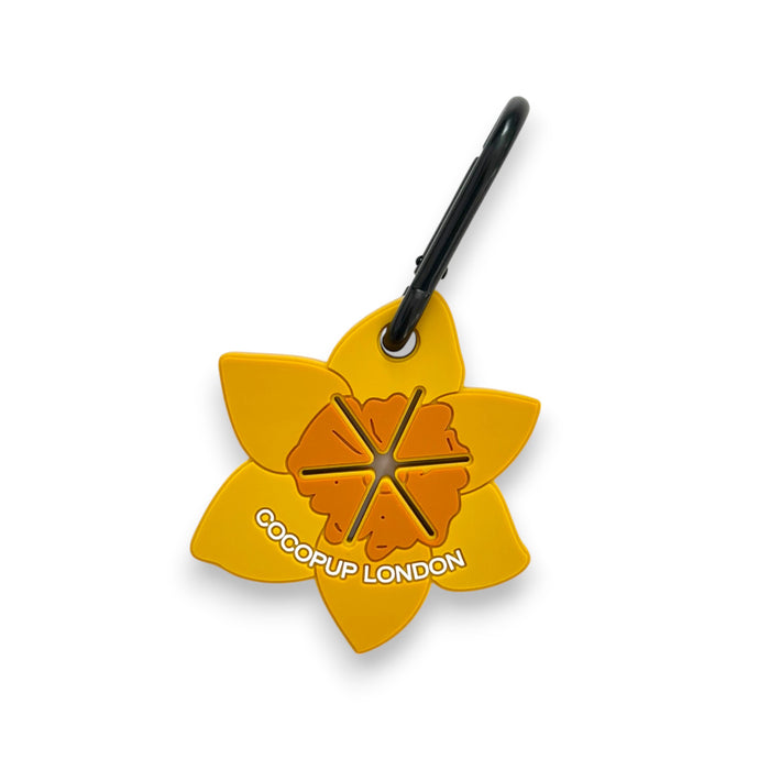 Yellow daffodil-shaped keychain with a black clip, designed for use with the Cocopup London CocoPOOP Pocket.