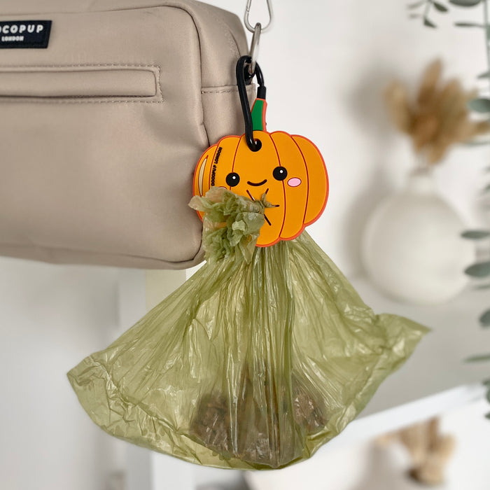 Pumpkin-shaped orange poop bag holder with a silver clip, designed for hands-free use on dog walks.