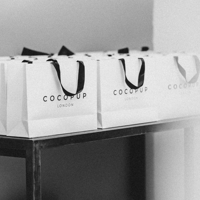 White Cocopup London gift bags with black ribbon handles, neatly lined up.