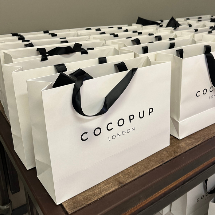 Cocopup London gift bags with black ribbon handles neatly lined up on a wooden table.