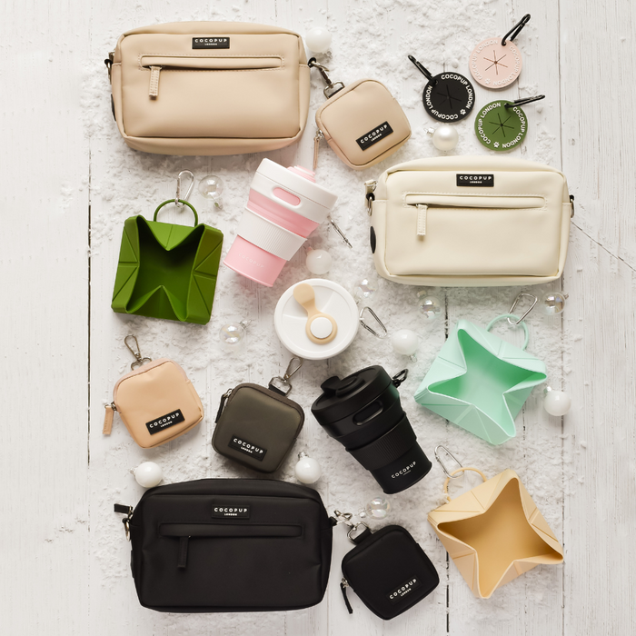 Khaki Cocopup London collapsible coffee cup, assorted bags, and a dog walk accessory on snow-covered wood.