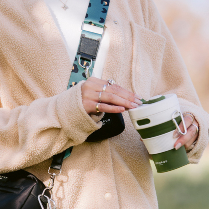Model holding the Cocopup Plain Khaki with White Lid Coffee Cup whilst wearing the Cocopup Black Dog Walking Bag.