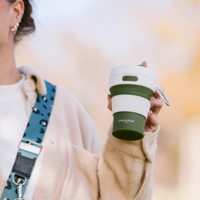 Model holding the Cocopup Plain Khaki with White Lid Coffee Cup whilst wearing the Cocopup Black Dog Walking Bag.