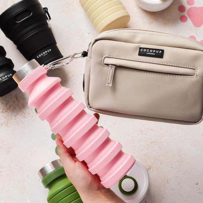 Pink Cocopup London collapsible water bottle held next to a beige Cocopup pouch on a light-colored surface.