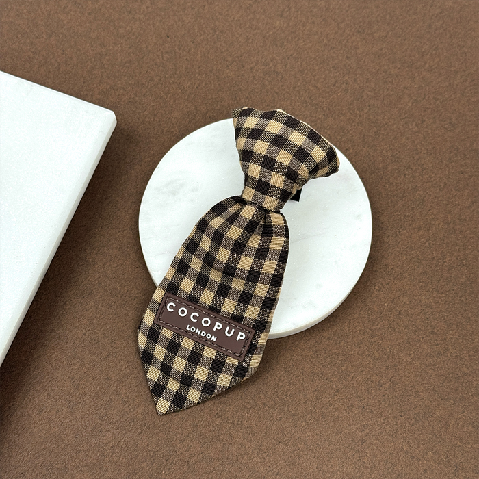 Brown and beige check dog tie displayed on a round white platform.