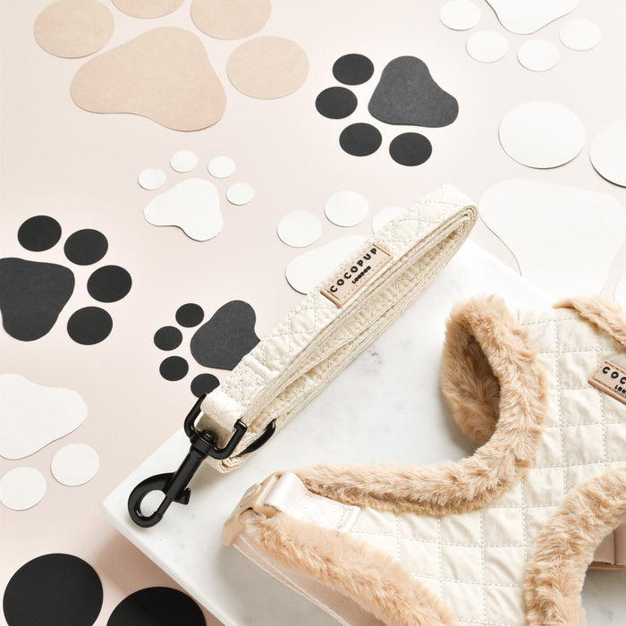 Cream quilted Cocopup London harness, lead, and collar set displayed on marble with paw print cutouts.