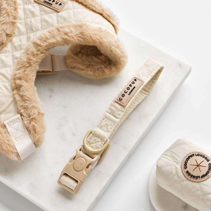 Cream quilted dog collar with safety lock, shown on a marble surface.