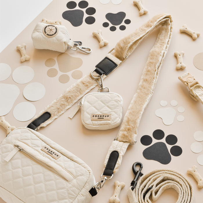 Cream quilted dog walking bag set with leash, treat pouch, and poop bag holder on a paw print background.