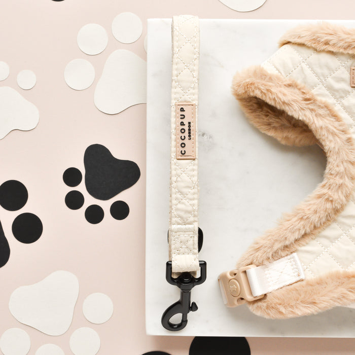 Cream quilted dog lead with fluffy trim, shown on marble surface with paw print cutouts.