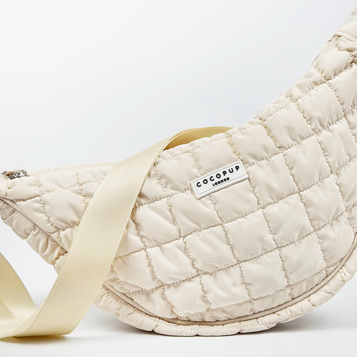 Cloud-colored crescent crossbody dog walking bag with a wide strap and front Cocopup London logo label.