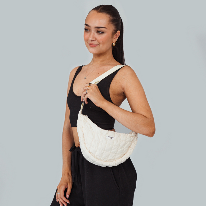 Woman in black holds a light grey Cocopup London crossbody dog walking bag against a plain light grey background.