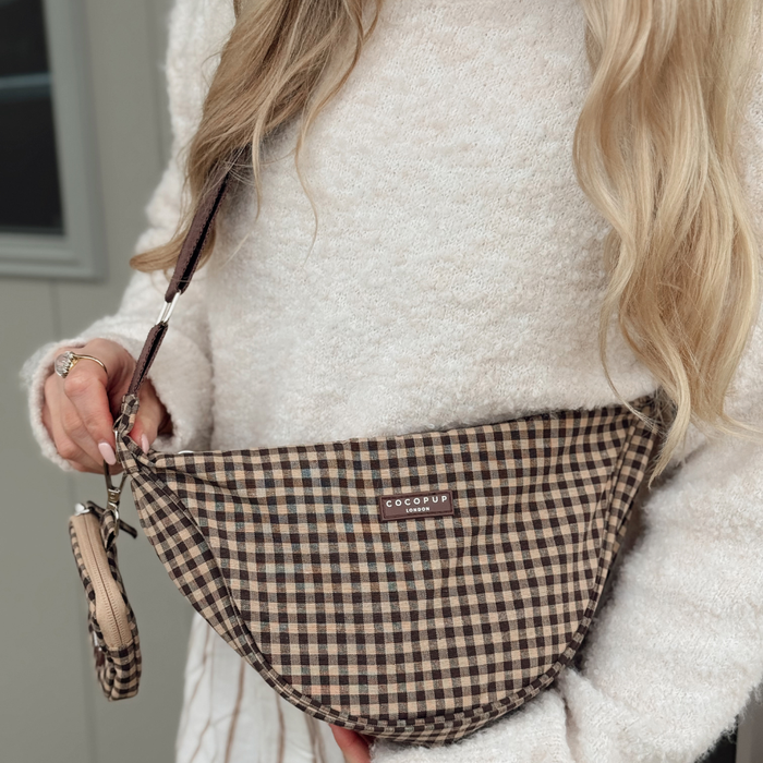 Woman in white sweater holds a check-patterned Cocopup London crossbody dog walking bag with matching poop bag dispenser.