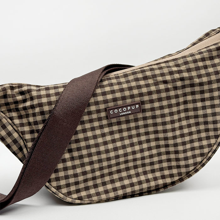 Cocopup London crossbody crescent bag in Cotswold check pattern with a dark brown strap and front logo label.