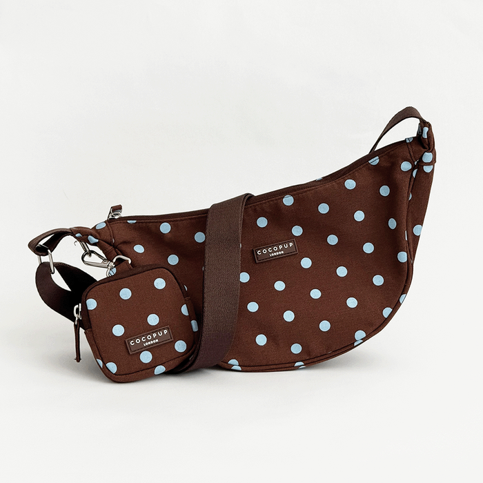 A brown fabric crossbody bag with a light blue polka dot pattern. Featuring Cocopup London logo badge and plain brown strap. Attached is a small matching treat pouch.