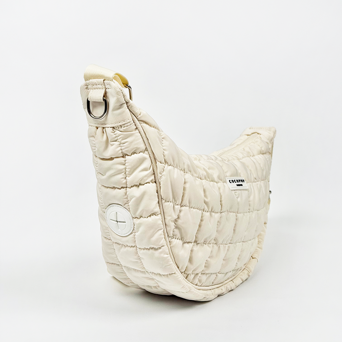 Cream quilted crescent crossbody dog walking bag with curved shape, displayed on a white background.